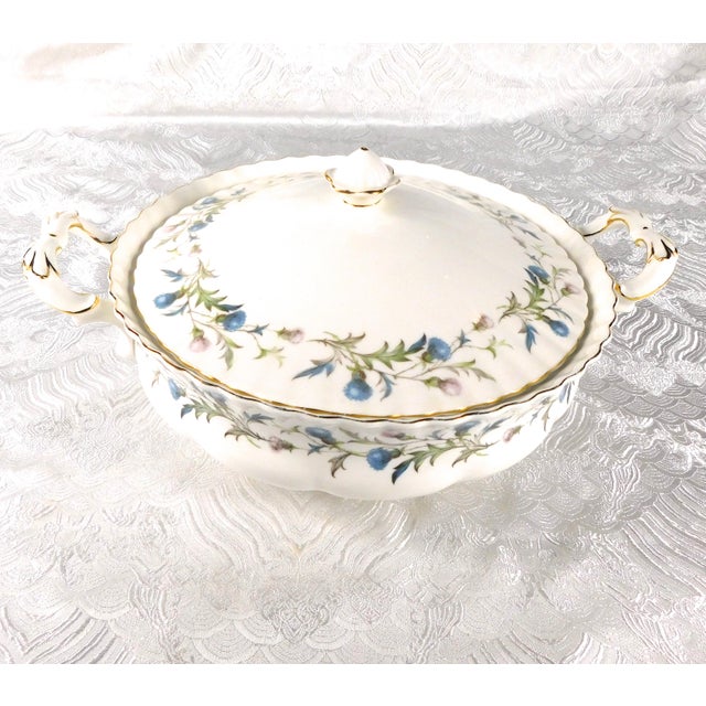 This is a round covered vegetable bowl by Royal Albert in Brigadoon. The piece is bone china from 1980. It is shiny white...