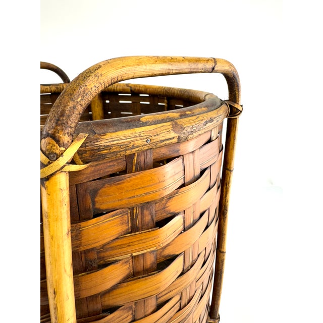 A substantial handwoven bamboo gathering basket featuring a tightly worked split weave and reinforced bentwood frame with...