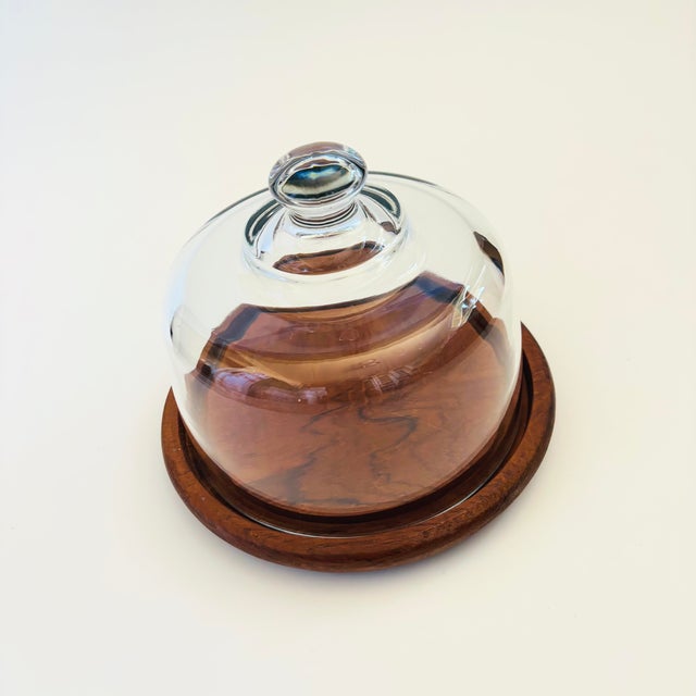 A vintage glass cloche. The top is made of heavy glass with an integrally formed handle sitting on a circular teak base. A...