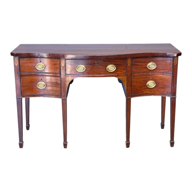A late 18th C. English George III mahogany serpentine-front sideboard with a shaped top above a central kneehole, flanked...