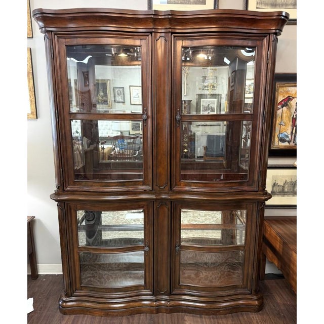 This elegant bombé-front china display cabinet features a richly finished wood frame, gracefully curved glass doors, and...