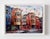 This mixed media piece captures a vibrant street scene, showcasing a charming row of buildings with intricate...