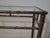 A chic Hollywood Regency–inspired console table featuring a metal frame crafted to resemble bamboo, finished in a warm...