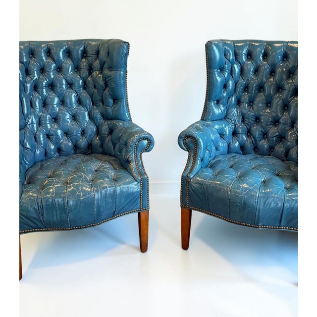 Striking pair of mid-century wingback chairs in original blue leather with deep button tufting, rolled arms and brass...