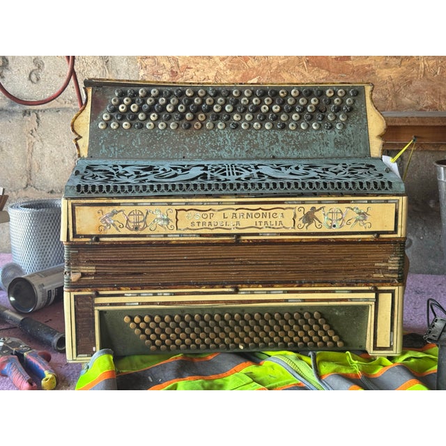 This is an antique button accordion made by Coop L'Armonica in Stradella, Italy. The instrument features intricate mother-...