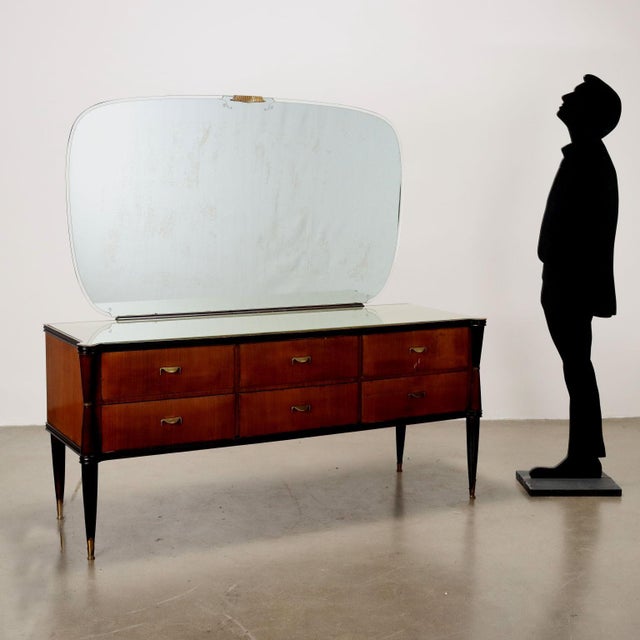 Cupboard with wooden drawers, back-treated glass top, mirror, brass handles and leg tips. This piece is attributed to the...