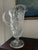 A striking vintage crystal pitcher featuring an elegant pedestal base, dramatic scalloped rim, and intricate cut-glass...