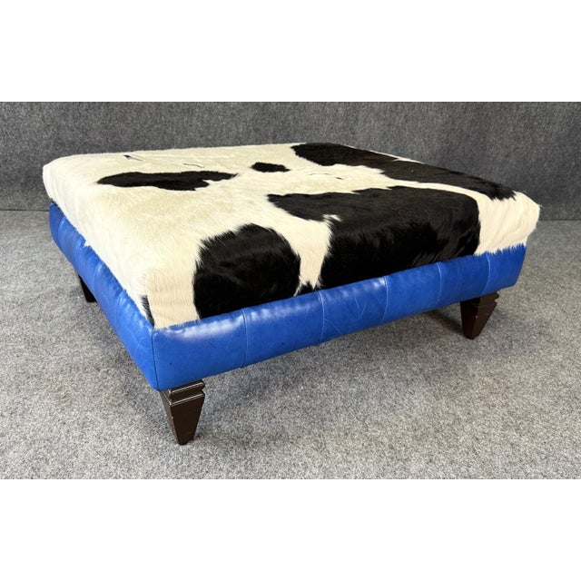 This Custom COCOCO Home Chesterfield ottoman features a bold black-and-white cowhide top paired with vibrant blue leather...