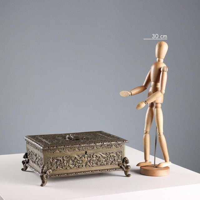 A chiseled bronze casket supported by four feet shaped like winged figures. All-over decoration of plant scrolls, birds,...