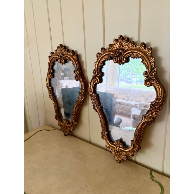 An elegant pair of Italian giltwood mirrors featuring richly carved Rococo frames with scrolling acanthus details and...