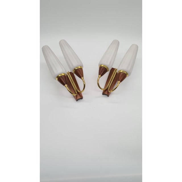 A pair of wall sconces from the 1960s, made in Germany from teak wood, brass, and frosted white glass. Each sconce has an...