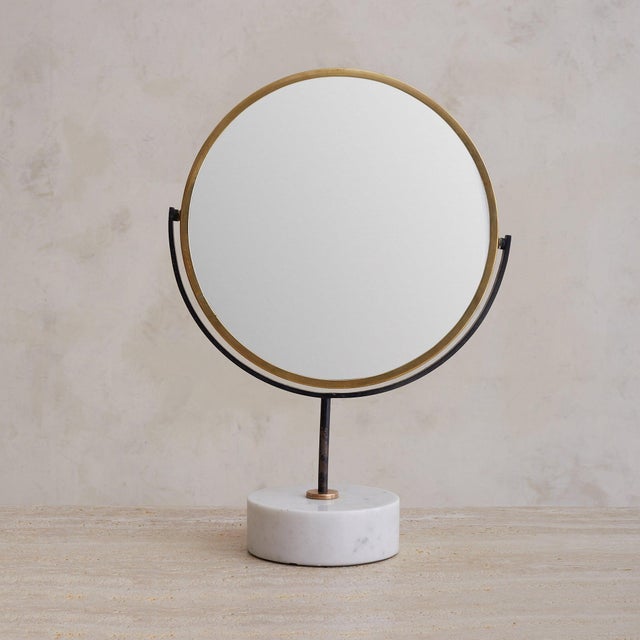 An Italian vanity mirror, circa 1950s. The round glass tilts within a slender brass frame, mounted on a blackened metal...
