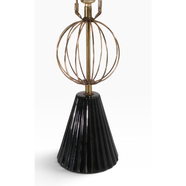 Classic Atomic style Mid Century table lamp, having a ribbed black ceramic cone shaped base, which supports a brass plated...