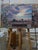This oil painting captures a solitary structure set against a vast, open landscape under a dramatic sky filled with soft...