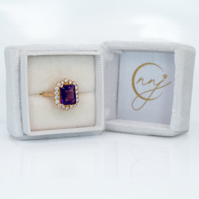 An amethyst takes centre stage in a deep royal purple at the heart of this solid 14K yellow gold ring, flanked by eighteen...