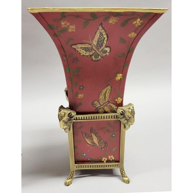 Decorative red tole vase with hand painted gold butterflies in brass stand with a ram's head on paw feet in each corner. A...