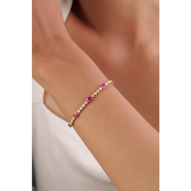 This tennis bracelet features 3.1 carats of natural oval-cut rubies, set in 14K yellow gold. Each ruby measuring...
