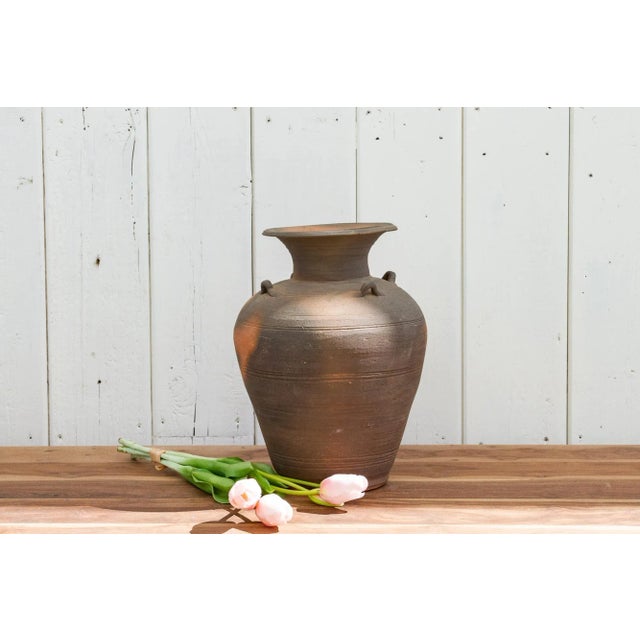 A tall country style Asian water vase found in Thailand. This rustic vessel has four miniature handles, a round body and a...