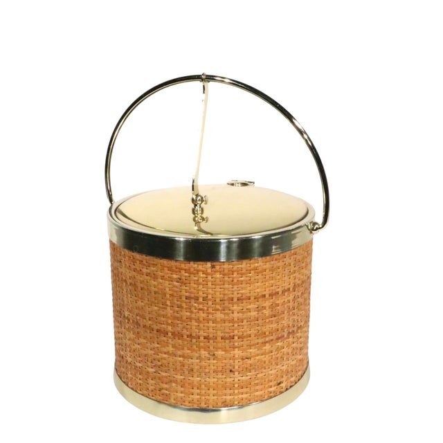 Chic and stylish Mid Century Hollywood Regency style ice bucket, having a raffia wrapped exterior, with a brass plated...