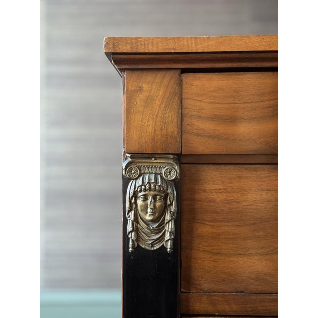 This French Empire chest of drawers carries the weight of history in every gilded detail. Dating back to the early 1800's,...