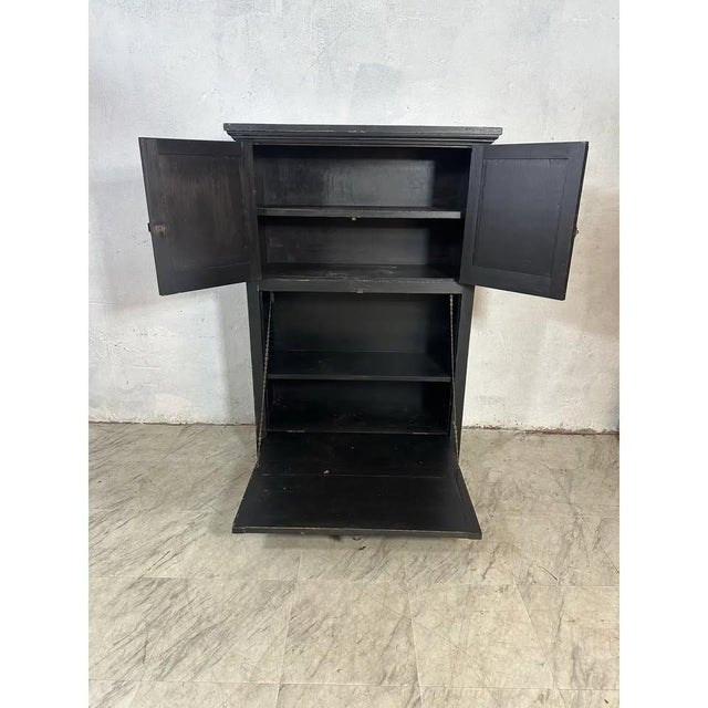 This is a vintage black-painted wooden cabinet with a drop-down door. It has a slightly distressed finish, giving it an...