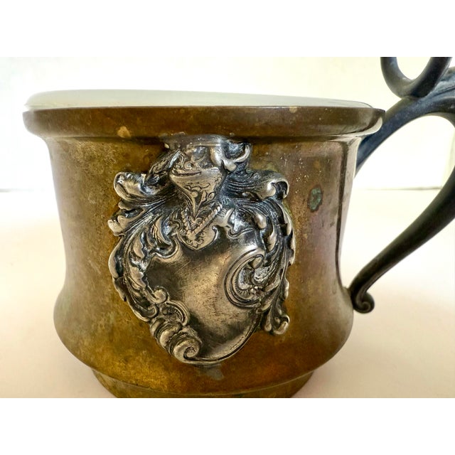 Dating to the early 20th century, this handsome gentleman's shaving mug features a warm brass body accented by a silver-...