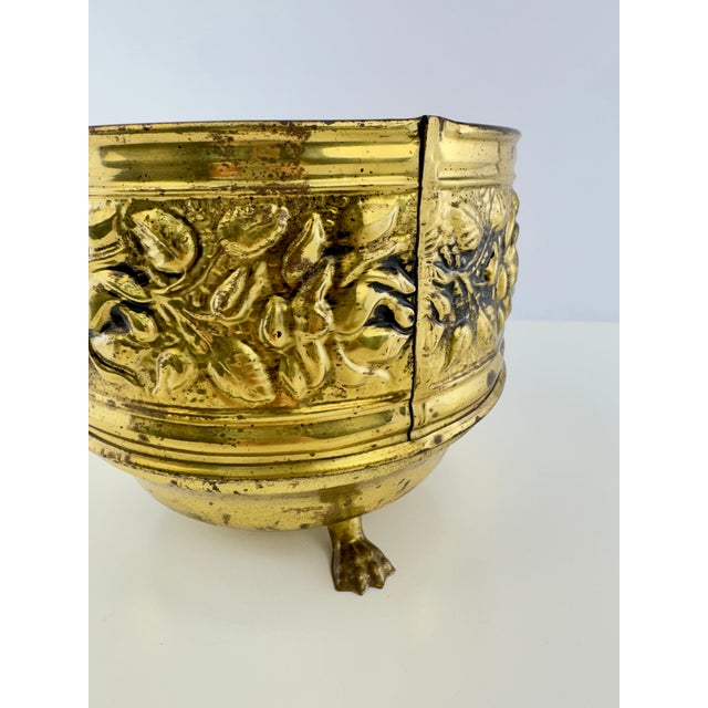 A richly detailed vintage English brass planter featuring a deeply embossed band of scrolling flowers and foliage. The...