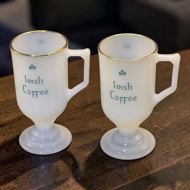 This product is a set of two vintage Irish coffee mugs made of milk glass with a shamrock pattern. The white mugs have a...