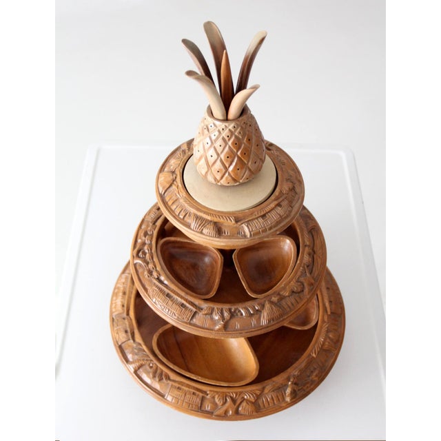A vintage mid-century tiered lazy Susan featuring intricately carved tropical motifs, a decorative pineapple finial, and...
