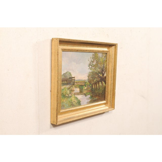 A French landscape painting in frame from the early 20th century. This antique painting from France depicts a tranquil...