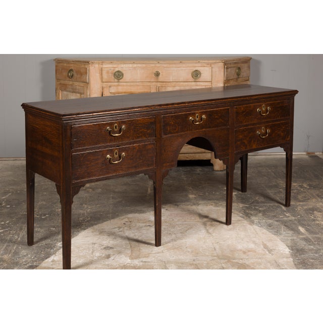 An English oak sideboard from the 19th century with five drawers, brass hardware, carved spandrels and straight legs....