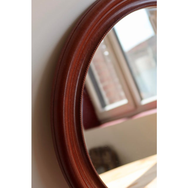Round mirror with a molded plastic frame in a dark wood-effect finish reminiscent of mahogany, featuring attractive...