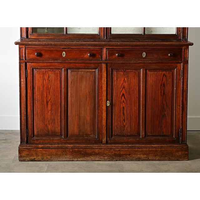 This French dark pine bookcase from the late 19th century makes a dramatic statement by its scale alone, and the crackled...