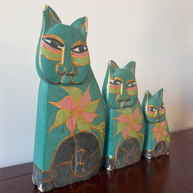Charming set of three hand-painted wooden cat figures featuring stylized faces and floral motifs. Each piece is...