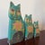 Charming set of three hand-painted wooden cat figures featuring stylized faces and floral motifs. Each piece is...