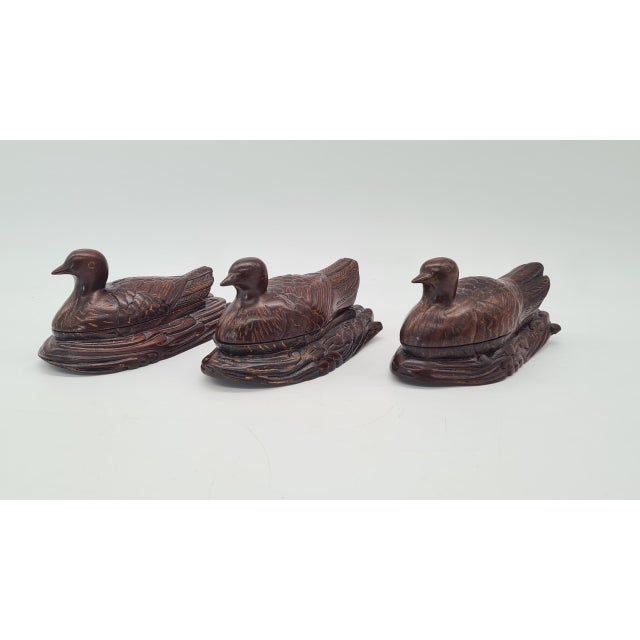 A unique set of three hand-carved wooden containers shaped like birds. Each piece is crafted from dark, decorative wood...