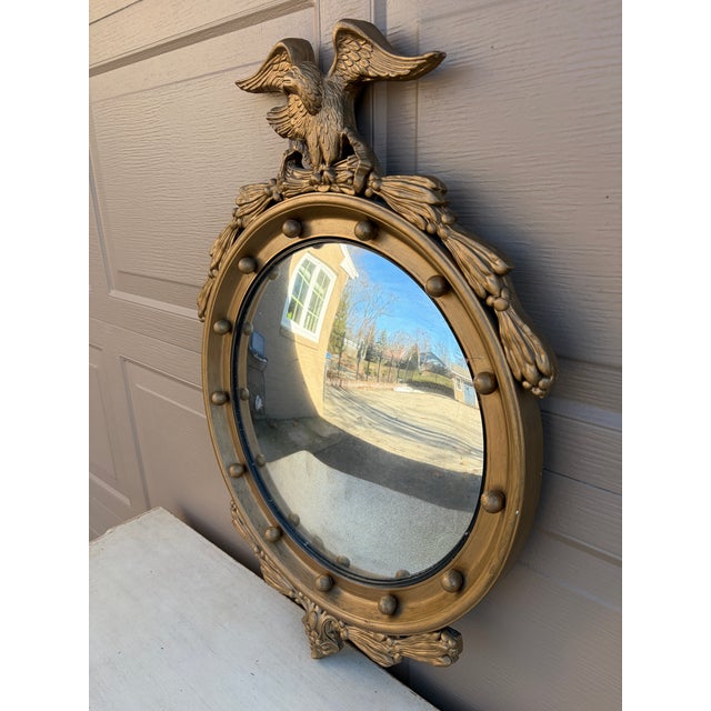 A gorgeous Federal or Regency style convex bullseye wall mirror featuring a carved eagle with open wings standing on olive...