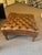 A well-proportioned, tufted leather ottoman or footstool upholstered in exquisite brown leather with deep button tufting...