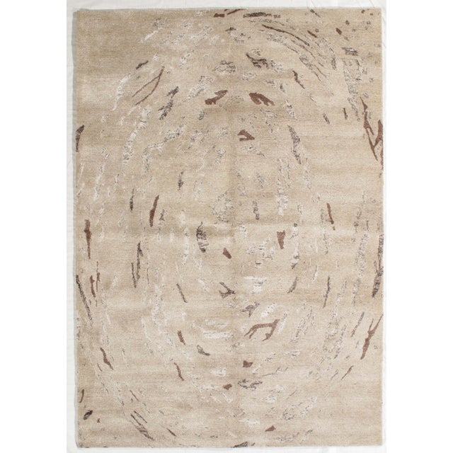 Hand-knotted modern rug featuring a soft, circular abstract composition with layered, swirling textures across a warm...