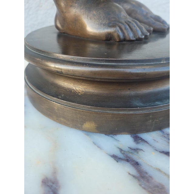 Patinated bronze sculpture of a standing winged putto, hands in front of the mouth Round base, wear to the patina and some...