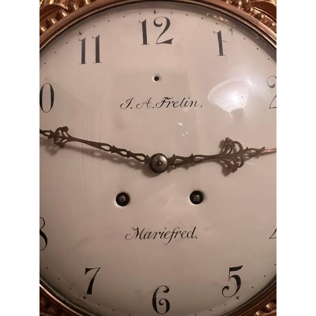 This elegant Gustavian-style wall clock features ornate giltwood craftsmanship, characterized by neoclassical motifs such...