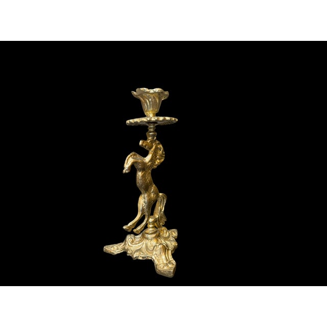 A single vintage brass candlestick modeled as a rearing horse, with a flower-shaped candle cup, scalloped drip tray, and a...