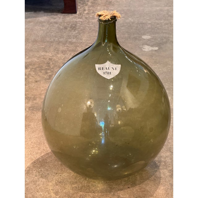A blown green glass demijohn with a shield reading "Beaune 1781." Cork stopper with burlap collar.