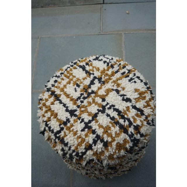 Cozy, modern pouf with a plush, textured fabric in a neutral cream base accented by black and warm brown tones. Supported...
