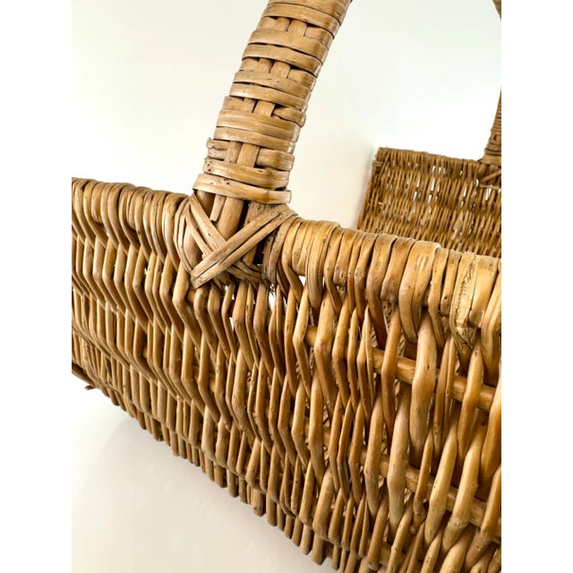 A vintage woven wicker log basket featuring a gracefully curved form and a tightly wrapped arched handle. Crafted from...