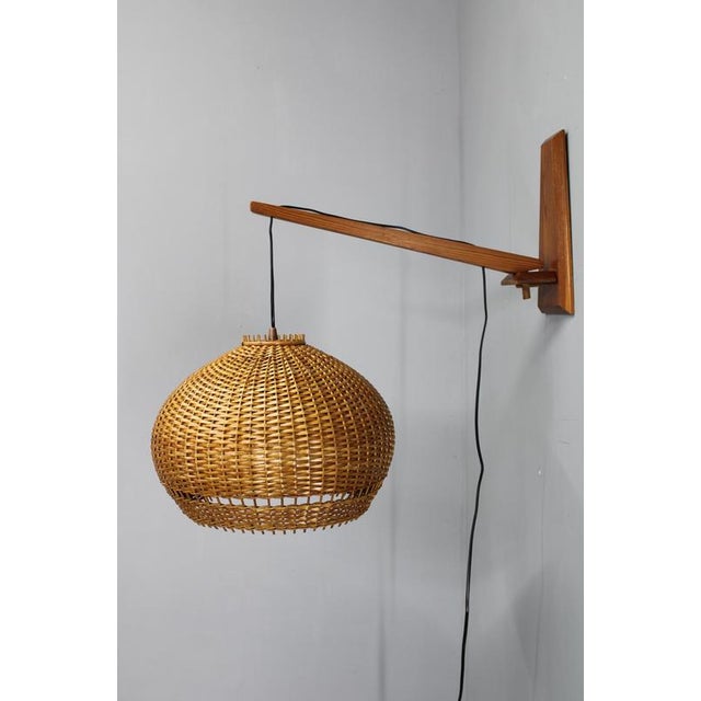 This adjustable wooden wall lamp with a hand-woven rattan shade was produced in czechoslovakia during the 1970s and...