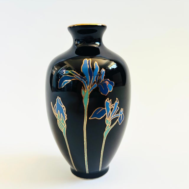 A petite glossy black vintage ceramic bud vase. Features a blue iris design outlined in metallic gold. Made in Japan by...