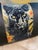 A lumbar cushion cover centered on a woven jacquard panel showing a black panther emerging from amber foliage and deep red...