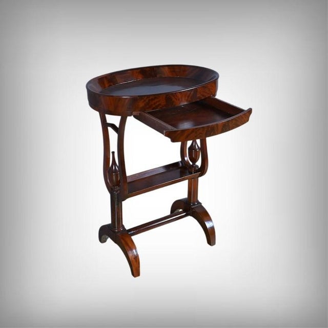An elegant Empire-style valet table, veneered in mahogany burl, revealing a warm patina with reddish highlights. The oval,...