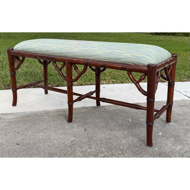 A striking faux bamboo bench featuring a sculptural wood frame with intricate decorative fretwork at the corners and a...